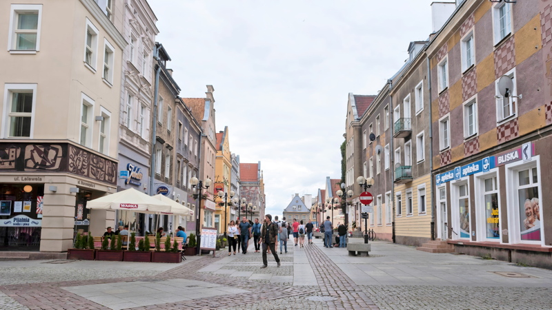 19 - Staromiejska Street in the Old Town of Olsztyn, featuring historic buildings, cobblestone pavement, outdoor seating, and pedestrians